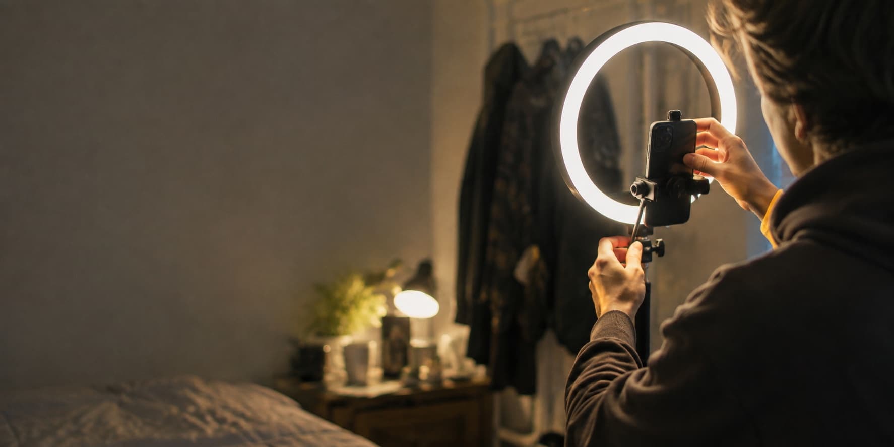 A creator angling a ring light and clipping a phone into its mount in a bedroom.