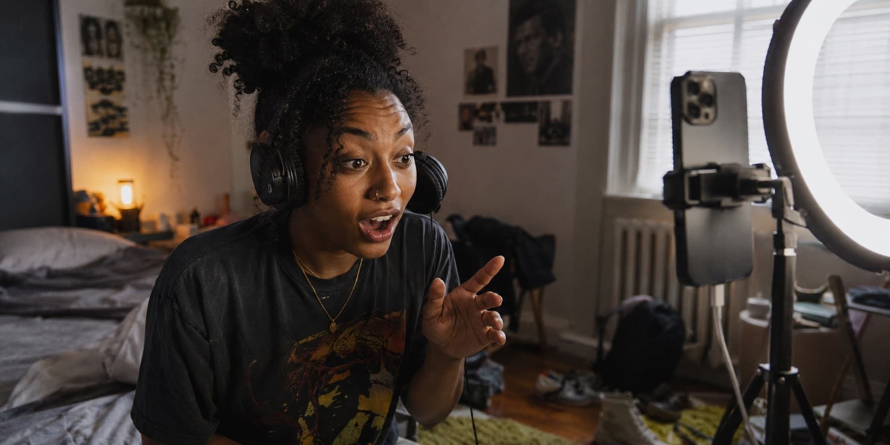 A creator in her bedroom, headphones on, reacting to a track as she films herself on a phone under a ring light.