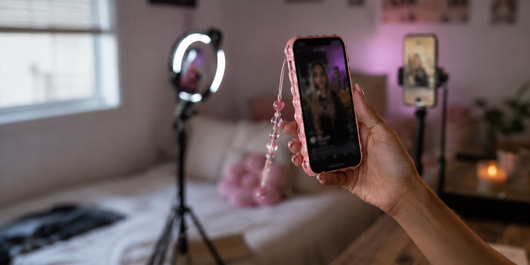 A hand holding a phone playing a vertical video, with more phones on stands out of focus behind it.